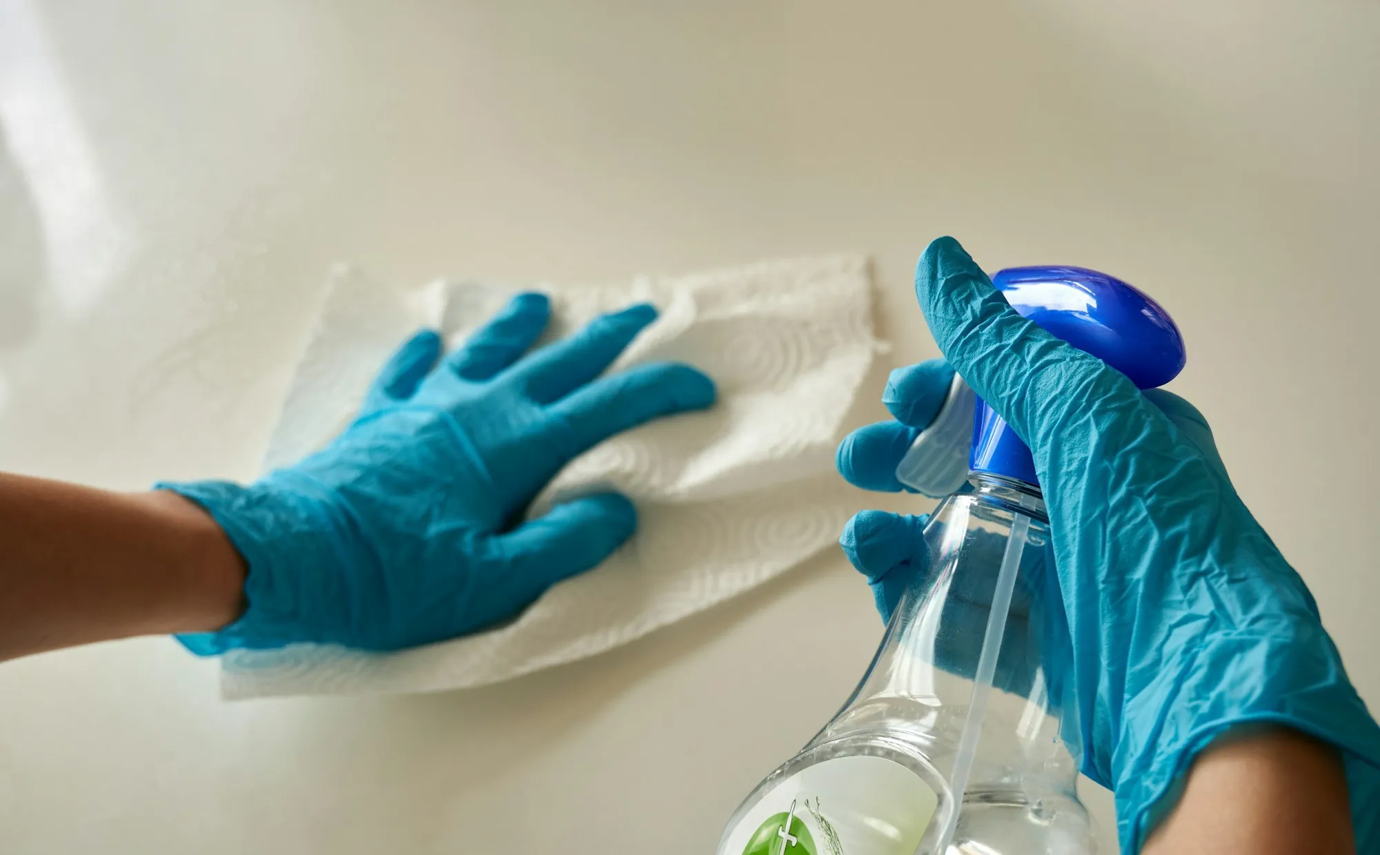 Gloved hands wiping a counter with a disinfectant spray